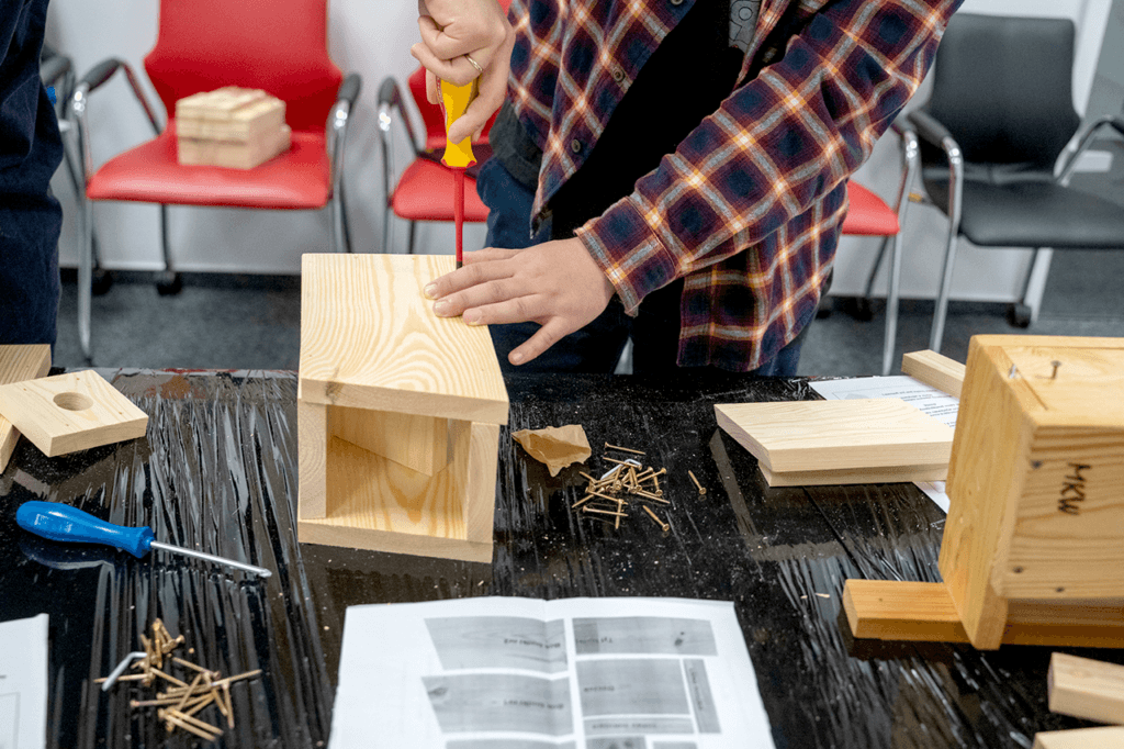 Na zdjęciu widoczny proces składania budki lęgowej dla ptaków przy pomocy śrubokręta, przez uczestnika warsztatów.