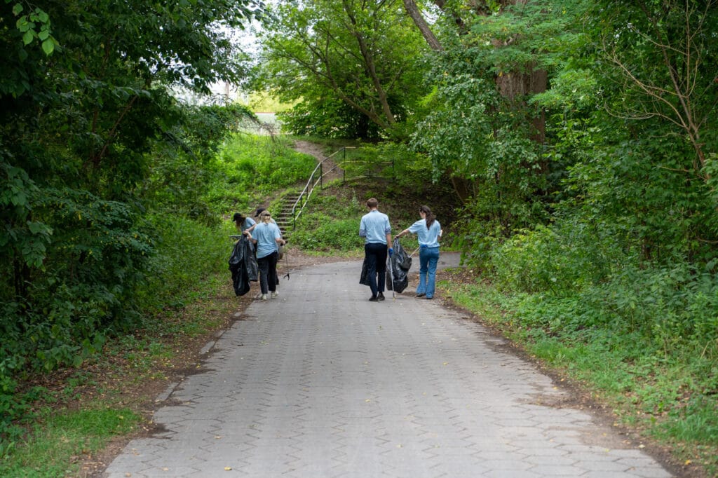 Sprzątanie z wolontariuszami - grupa osób zbierających śmieci na alejce. 