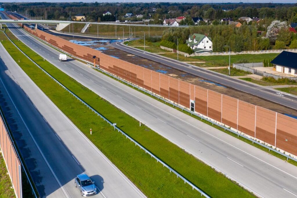 na zdjęciu widoczna autostrada z ekranami akustycznymi. ma ona zapobiegać zanieczyszczeniu okolicznych gospodarstw domowych hałasem